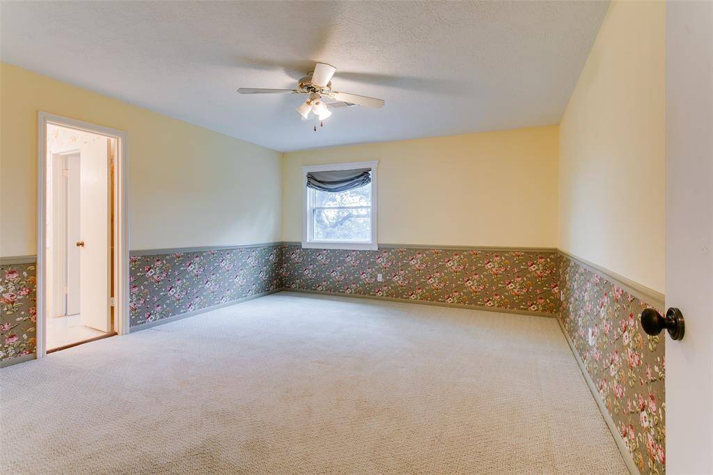 The third bedroom is spacious, well lit with floral wallpaper bottom, light carpet, and ceiling fan. It shares the Jack and Jill bathroom.