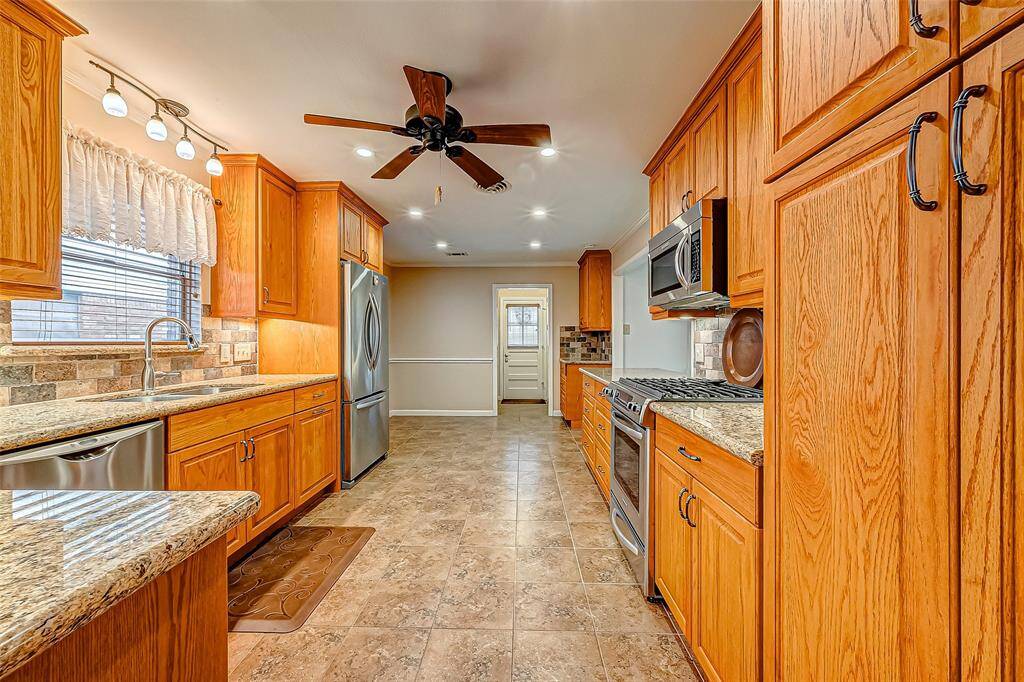 This generously sized kitchen showcases custom wood cabinetry with pull out drawers, sleek granite countertops, and contemporary stainless steel appliances. A ceiling fan, abundant natural light, and elegant tile flooring enhance its welcoming and practical design.