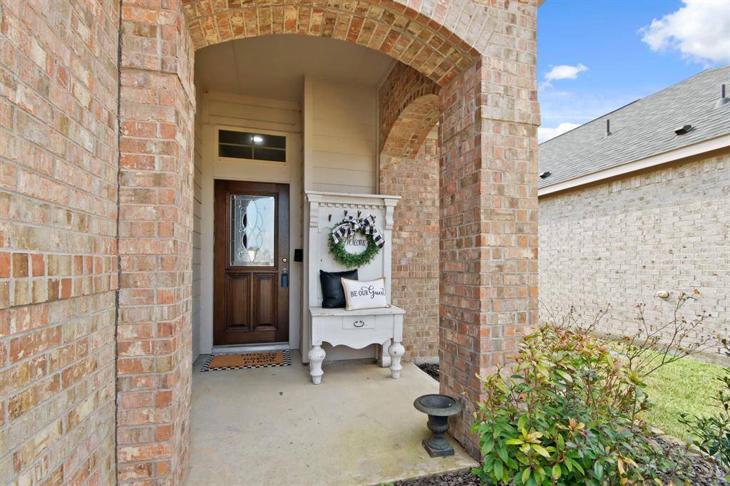This photo showcases a welcoming front porch with a charming brick archway. The entrance features a decorative wooden door with a glass insert.