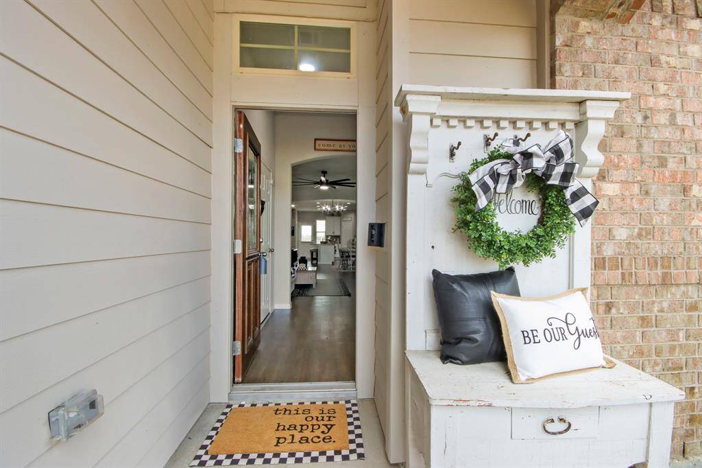 Welcoming entrance on this covered entryway. The open door reveals a glimpse of a spacious, well-lit interior with hardwood floors and a ceiling fan. Cozy and inviting atmosphere.