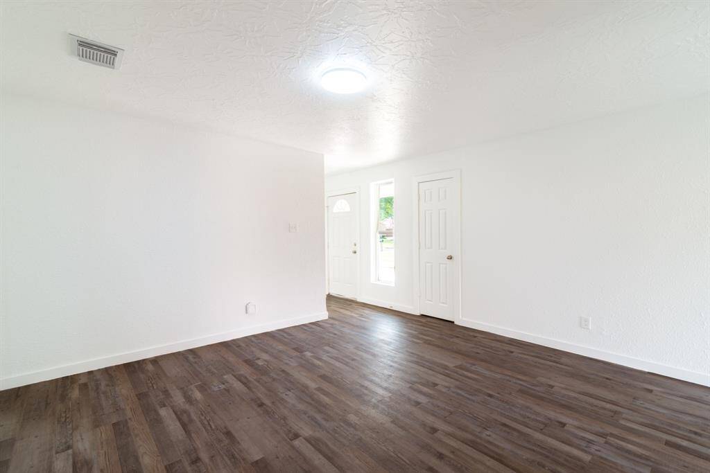 This photo shows a single-story home with a clean white exterior and a spacious driveway leading to a two-car garage. The front yard is well-maintained with green grass, and the house features large windows, giving it a bright and inviting appearance.
