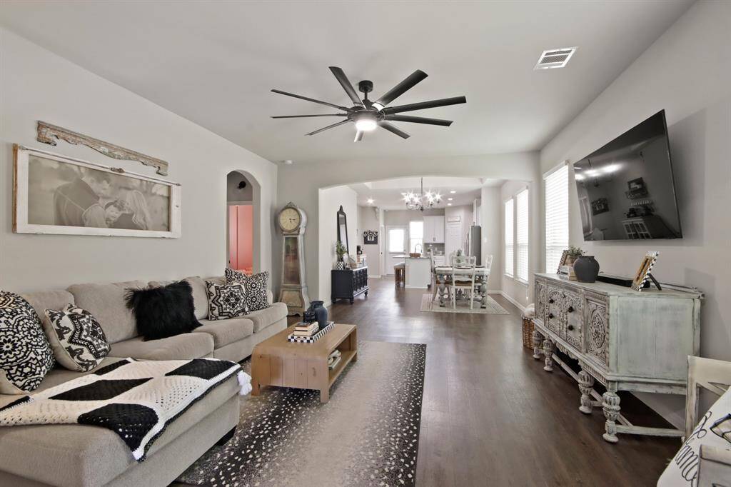 This photo showcases a modern, open-concept living and dining area with sleek wood look vinyl flooring. A ceiling fan adds a contemporary touch, and natural light fills the room through multiple windows, creating a bright and inviting atmosphere.