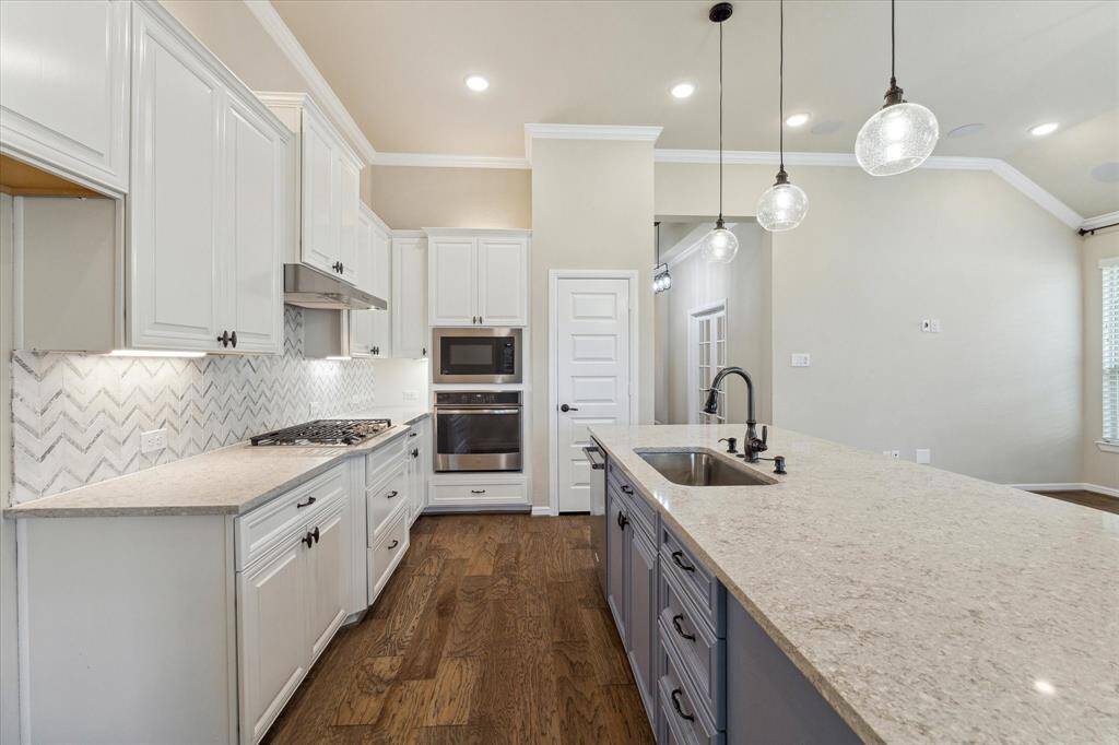 Most of the drawers have metal pull out trays for easy storage, there are pots and pans drawers too, 5 burner cooktop, stainless steel appliances, pendant lights over island and the kitchen is crisp and neat.