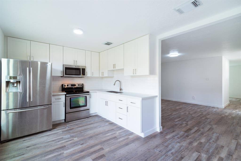 Bright and spacious room with sleek wood flooring and white textured walls. It features a modern ceiling light and ample natural light from a window near the entrance.