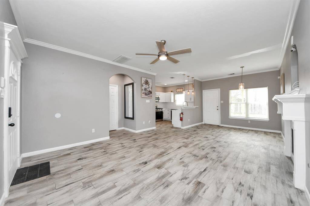 Bright living room with modern flooring, neutral gray walls, and a cozy fireplace. Features a ceiling fan, large windows for natural light.