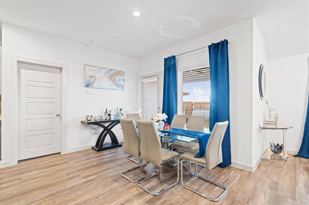 This is a modern and bright dining area featuring neutral color palette and premium laminate flooring. Natural light streams in through the window, enhancing the room's airy ambiance. Approximate Measurements: 11X10
