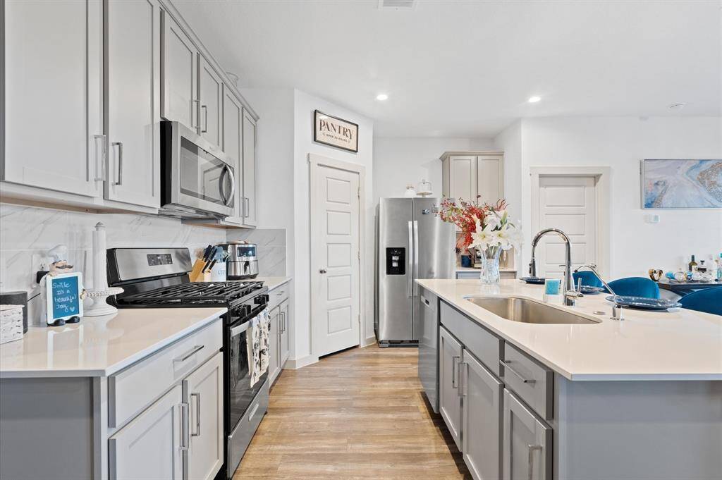 This is a bright, modern kitchen featuring stainless steel appliances, white subway tile backsplash, and white shaker-style cabinetry with sleek hardware. A spacious island with a sink provides additional counter space, and there's a designated pantry area for storage. The kitchen is finished with premium laminate flooring that adds warmth to the clean, contemporary design. Side-by-side refrigerator is included. Approximate Measurements: 17x11
