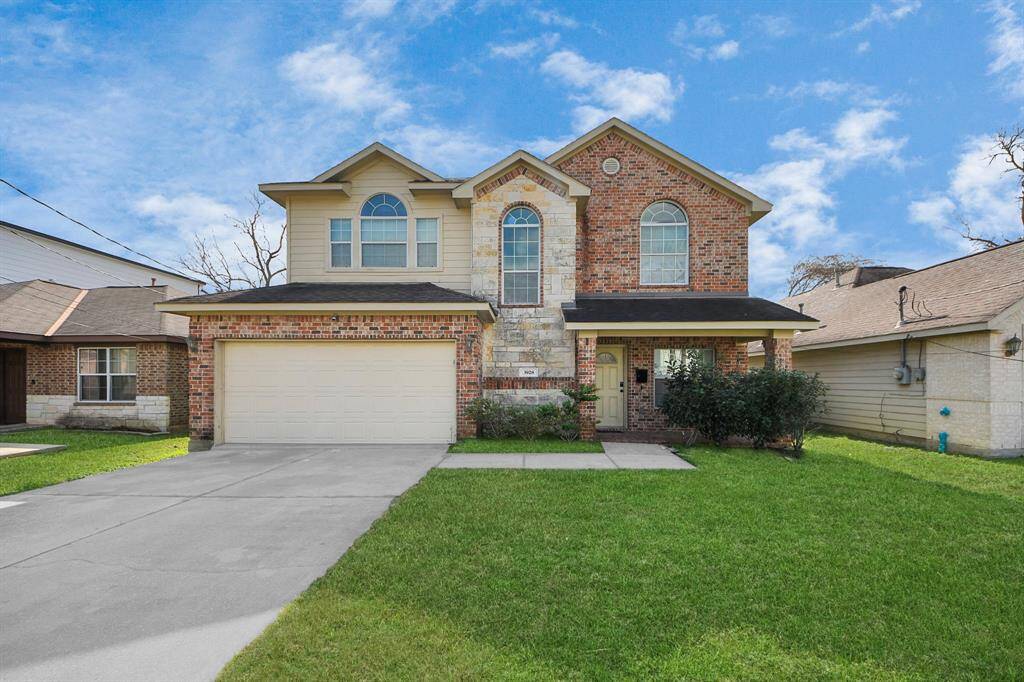 This two-story brick home has a double garage and a well-maintained front yard. It features large, arched windows and a covered entryway.