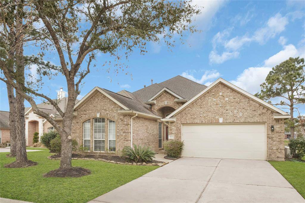 This charming home features a brick exterior, a spacious driveway leading to a two-car garage, and a well-maintained front yard with mature trees and shrubs, offering great curb appeal.