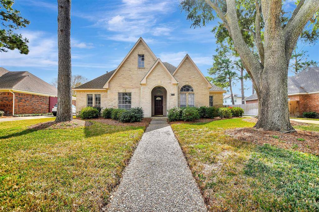 Welcome to this charming brick home on a spacious lot with a steep gabled roof, nestled between mature trees. It features a welcoming pathway, manicured lawn, and shrub-lined entrance. Ideal for a cozy family setting.