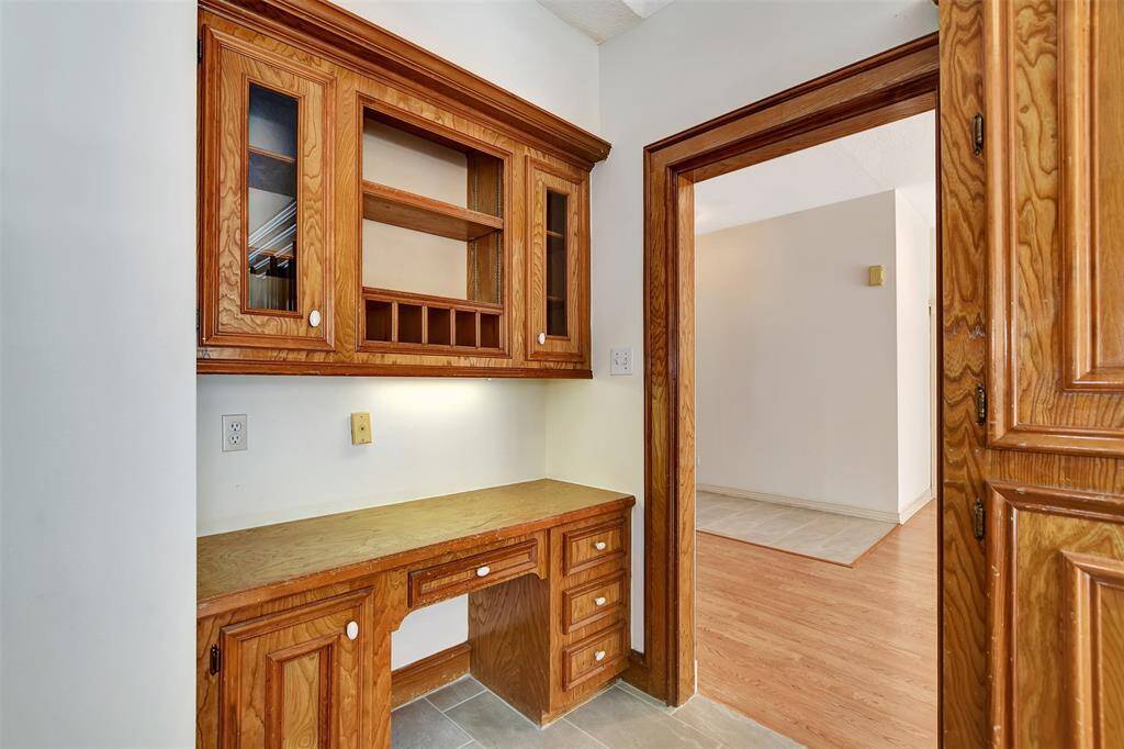 This photo shows a small nook with built-in wooden cabinetry, perfect for a home office or storage. It features a countertop with drawers and overhead cabinets with glass-paneled doors.