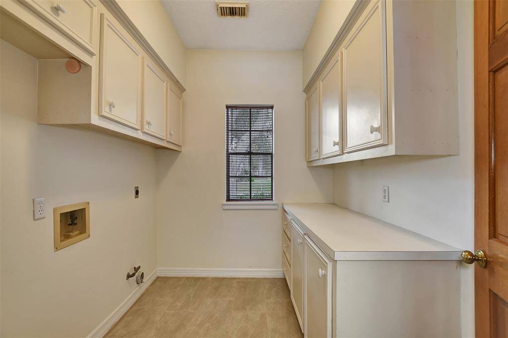 This photo shows a laundry room with ample cabinetry for storage, a countertop for folding clothes, and hook-ups for a washer and dryer. It has a window for natural light and a neutral color scheme.