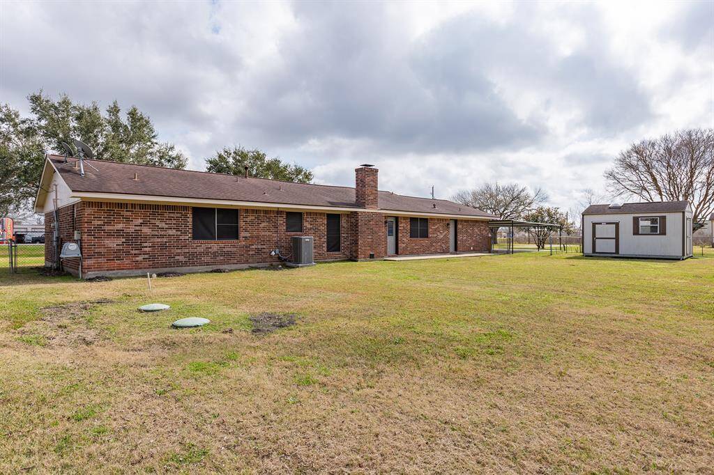 This photo shows the backyard of a brick house with a spacious lawn. It includes a small shed in the fenced in area and provides ample outdoor space.