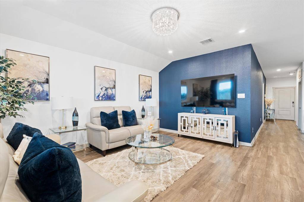 This is a modern and spacious living room with elegant premium laminate floors and a striking blue accent wall. It features a crystal chandelier, contemporary furnishings, and tasteful artwork, creating a stylish and comfortable space. Approximate Measurements: 16x14