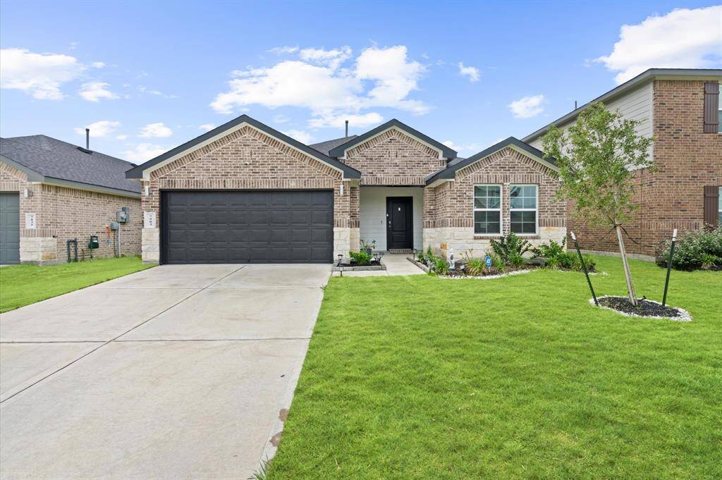 This is a single-story, brick facade home featuring a two-car garage and a well-manicured lawn. The house has a welcoming entryway with a pathway leading to the front door.