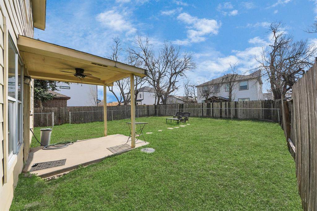 Spacious backyard featuring a covered patio with a ceiling fan, perfect for outdoor relaxation. The yard is enclosed with a wooden fence, providing privacy and a safe space for activities.