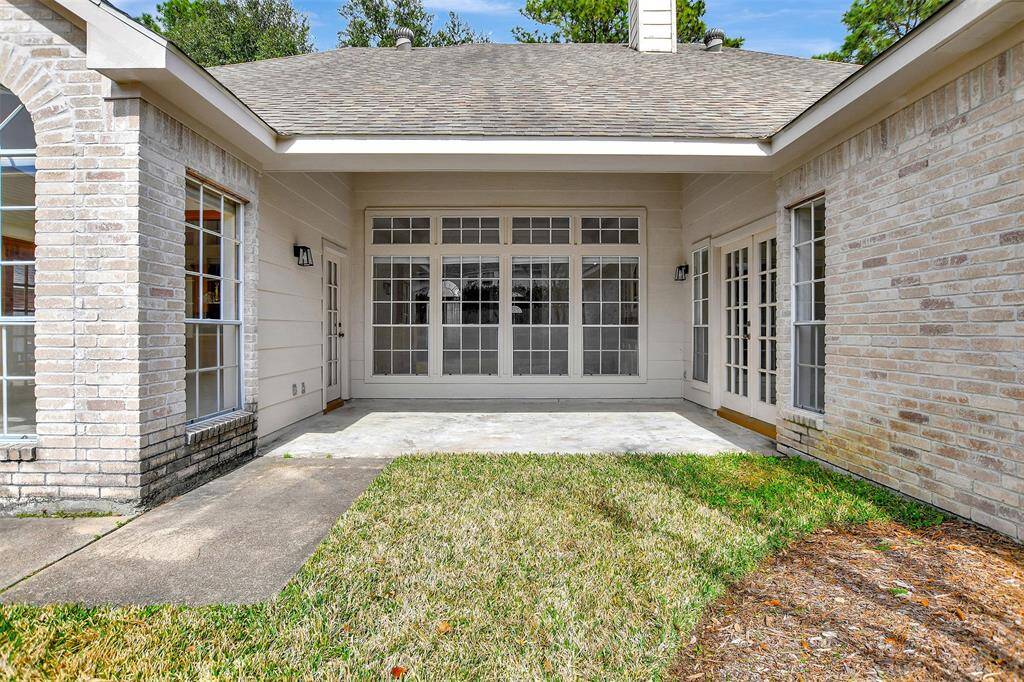 This photo showcases a cozy backyard patio area with a small grassy section. The space is surrounded by light brick walls and features large windows and French doors, providing ample natural light and a seamless indoor-outdoor connection. Ideal for relaxation or entertaining.