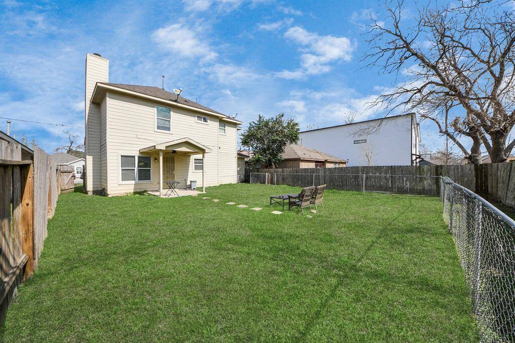 Spacious backyard with lush green grass, featuring a two-story house with a covered patio. The yard is fenced, offering privacy and a cozy outdoor seating area, perfect for relaxation or entertaining.