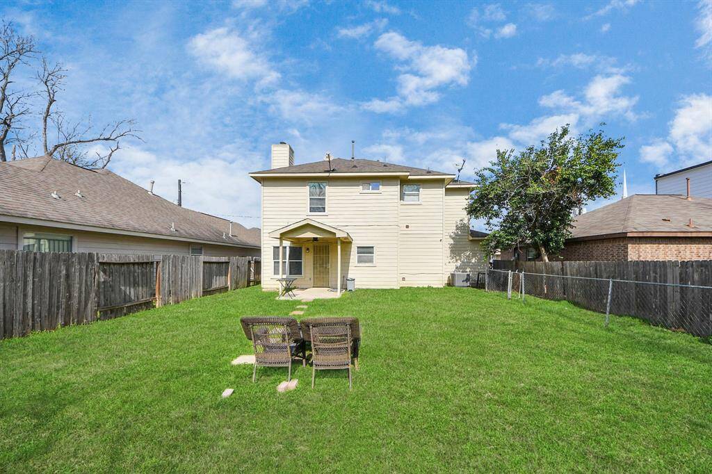 Spacious backyard with lush green grass, featuring a two-story house with a covered patio. The yard is fenced, offering privacy and a cozy outdoor seating area, perfect for relaxation or entertaining.