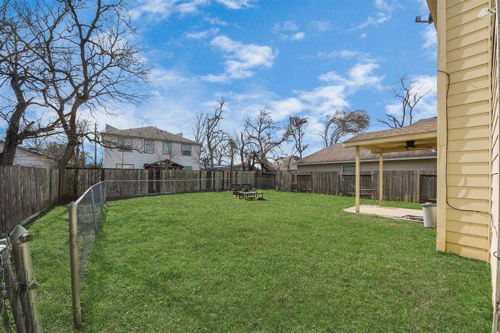 Spacious backyard with lush green grass, featuring a two-story house with a covered patio. The yard is fenced, offering privacy and a cozy outdoor seating area, perfect for relaxation or entertaining.