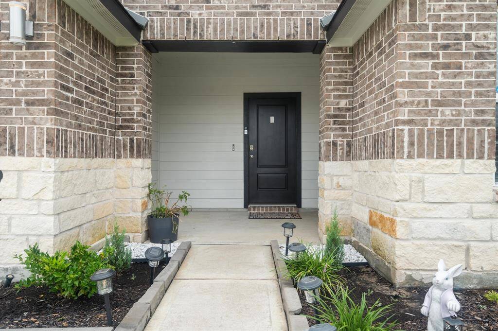 The entrance features a covered porch accented by a two-tone brick facade, complemented by stone detailing. A welcoming black front door is framed by well-maintained landscaping, adding to the home's curb appeal.