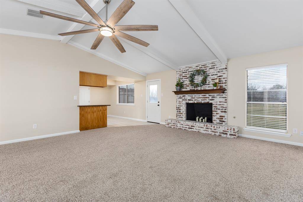 Spacious living room featuring a charming brick fireplace (wood burning or gas), vaulted ceilings, and abundant natural light, perfect for cozy gatherings.