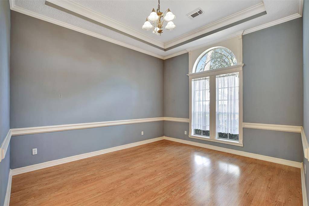 This room features elegant hardwood floors, soft blue/gray walls with white trim, and a large arched window that lets in plenty of natural light. A classic chandelier hangs from the tray ceiling, adding a touch of sophistication. Ideal for a dining or sitting area.