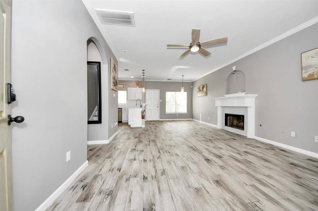 The living room is bright with modern flooring, neutral gray walls, and a cozy fireplace. It also features a ceiling fan and large windows for natural light.