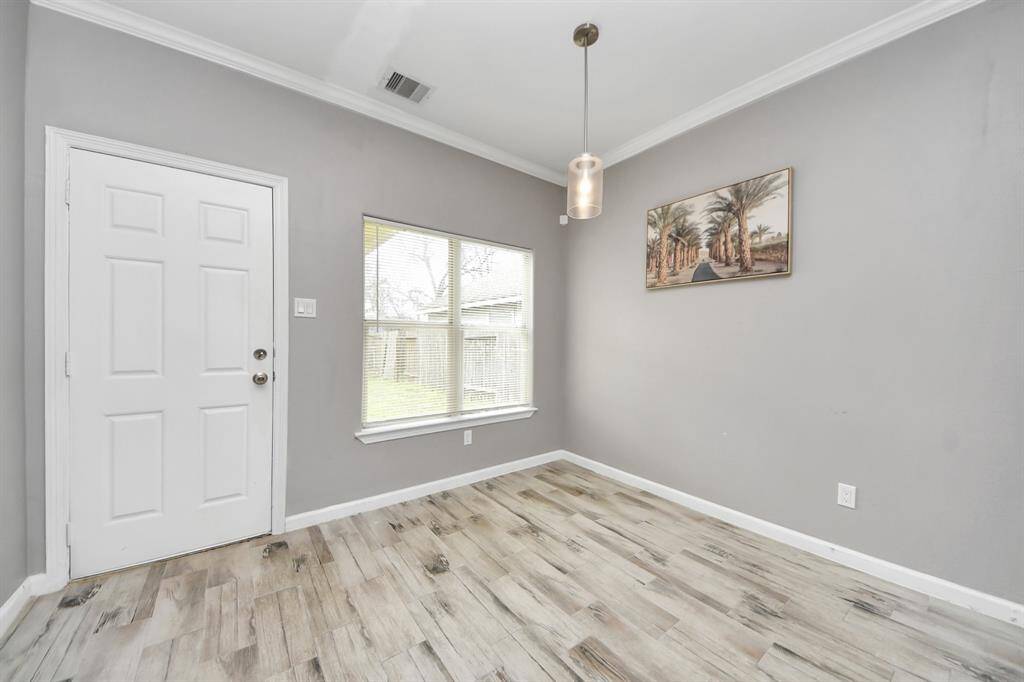 Bright living room with modern flooring, neutral gray walls, and a cozy fireplace. Features a ceiling fan, large windows for natural light.