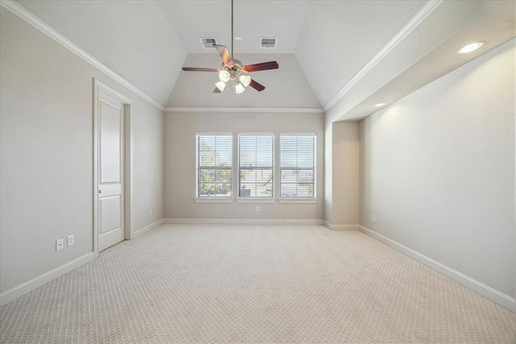 Spacious bedroom with vaulted ceiling, neutral carpet, and natural light from large windows. Features a ceiling fan and recessed lighting.