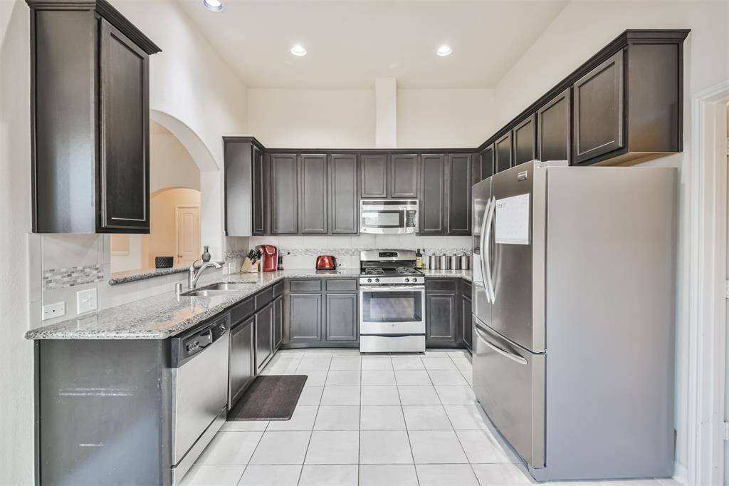 The kitchen boasts elegant granite countertops, modern stainless steel appliances, and tall cabinets adorned with crown molding for a polished finish.