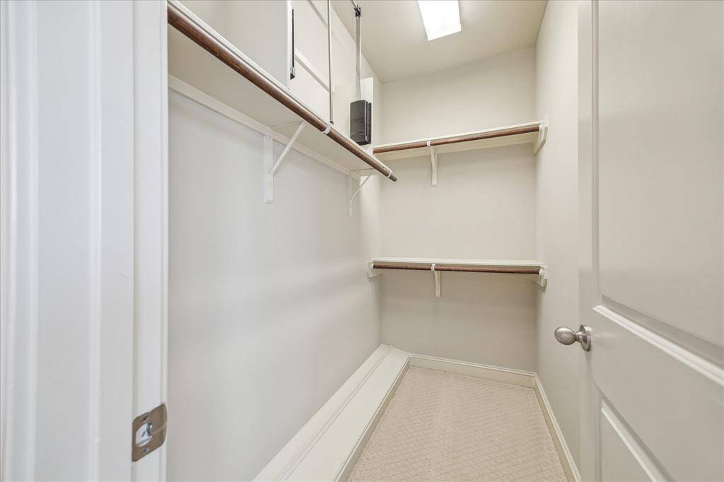 This is a spacious walk-in closet with multiple shelves and hanging rods, featuring neutral walls and carpet flooring, providing ample storage space.