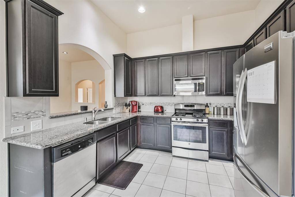 The kitchen features soaring ceilings, a stylish tile backsplash, and a double undermount sink for added functionality and elegance.