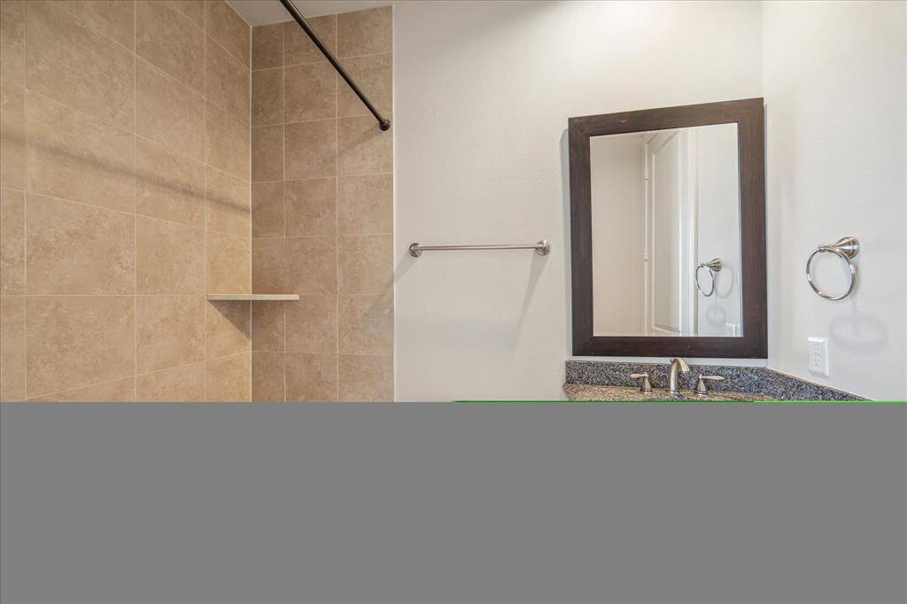 This bathroom features a spacious walk-in shower with beige tile, a sleek vanity with a granite countertop, and a large framed mirror. Modern fixtures and neutral tones create a clean and inviting space.