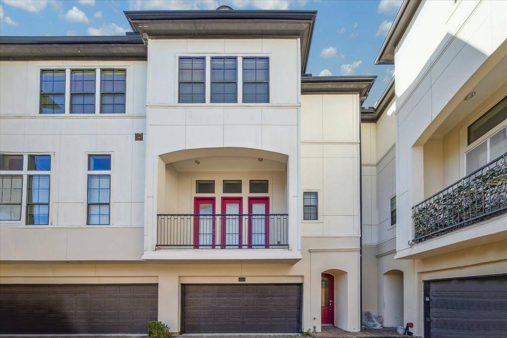 This townhouse features a modern facade with clean lines, large windows, and a two-car garage. The entryway includes a charming balcony and vibrant red doors, adding a touch of character to its contemporary style.