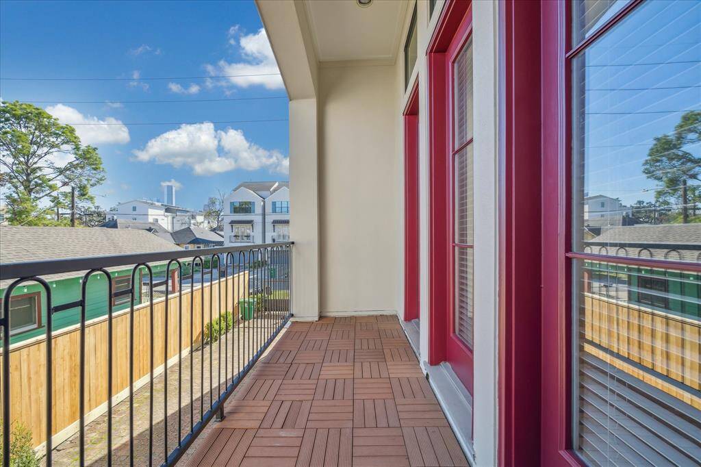 This photo showcases a cozy balcony with wooden flooring and red-framed glass doors, offering a pleasant city view and clear skies. Perfect for enjoying outdoor relaxation.
