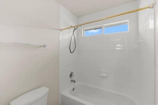 This photo shows a bright, spacious room with light-colored walls and flooring. It features a ceiling light fixture, a closed door, and two open doorways leading to other areas, suggesting good flow between spaces.