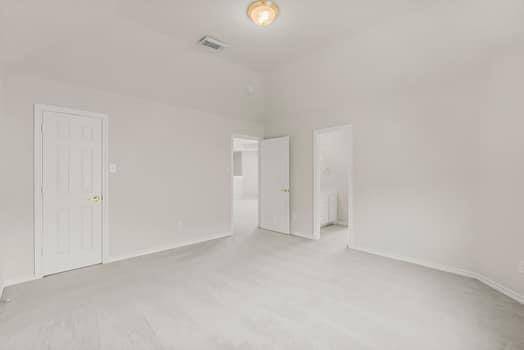 This photo features a bright bathroom with a vanity and large mirror, complemented by ample lighting above. A doorway leads to a sunlit room with a large arched window, offering a view outside. The space is clean and fresh, with neutral colors.