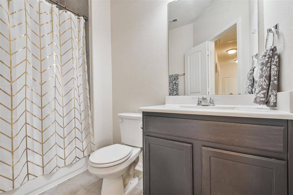 The hall bathroom features a cultured marble vanity, an elongated toilet, and a tub/shower encased in elegant ceramic tile.