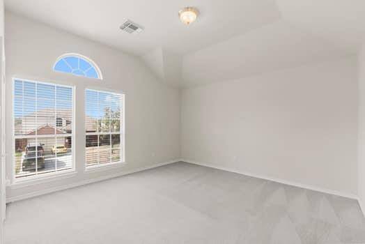 Bright, spacious bedroom with neutral walls and carpet, a vaulted ceiling, and a large window offering natural light and outdoor views. Features a large closet.