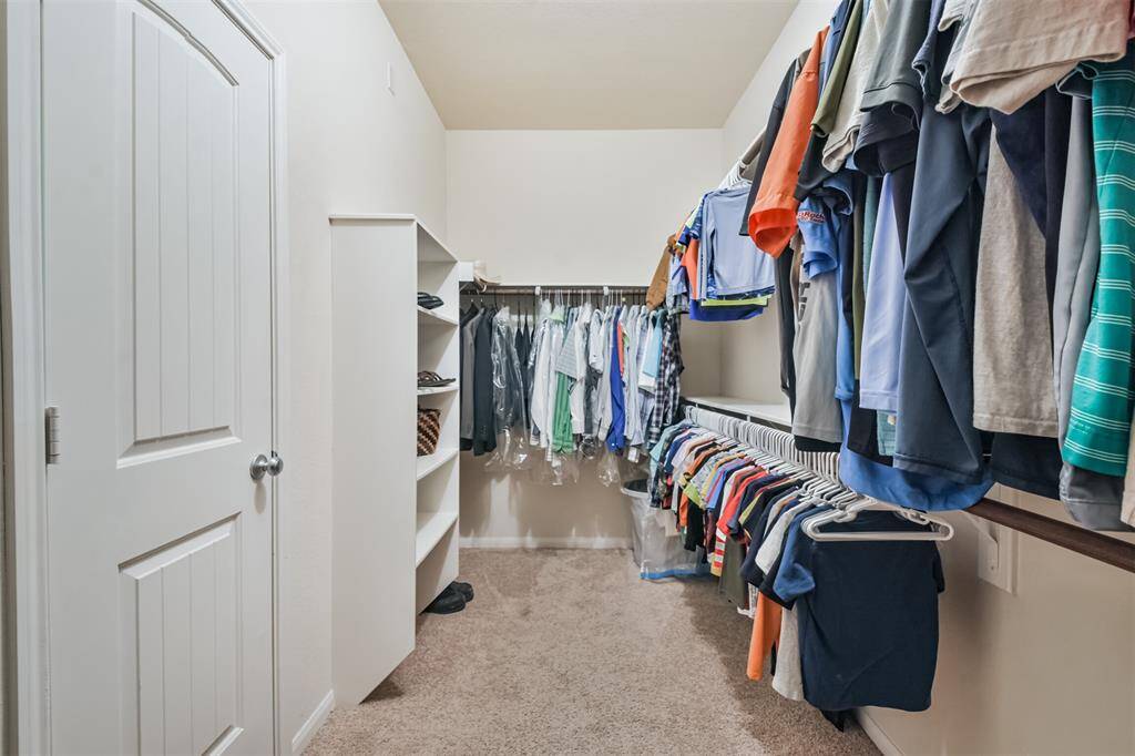Spacious walk-in closet featuring built-in shelving and sturdy wooden rods for hanging clothing, offering ample storage and organization.