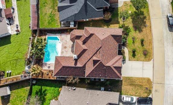 This photo showcases a spacious backyard featuring a covered patio with a ceiling fan, overlooking a swimming pool. The area is fenced for privacy and includes tropical landscaping, perfect for outdoor enjoyment and relaxation.