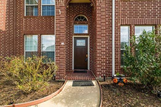 This photo shows the entrance of a classic brick home with a welcoming updated front door framed by large windows. The pathway is lined with simple landscaping, providing a neat and inviting approach to the house.
