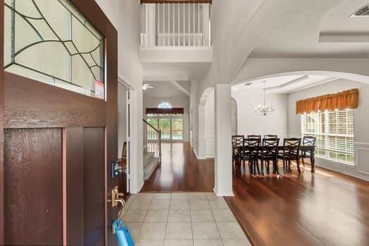 This welcoming home features a bright and open entryway with a tiled floor leading to a spacious dining area with wooden flooring. The large windows provide ample natural light, and the high ceilings add to the sense of space. A staircase and additional rooms are visible, enhancing the open layout.