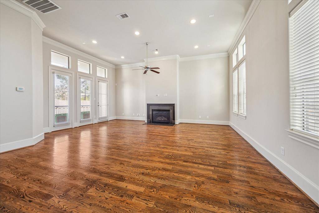 This spacious living room features beautiful hardwood floors, large windows for ample natural light, and a cozy fireplace. High ceilings and neutral walls create an airy, inviting atmosphere, perfect for relaxation or entertaining.