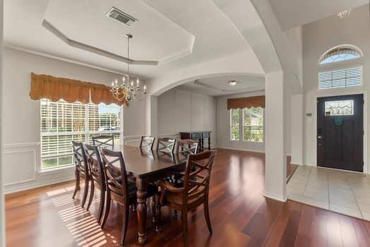 Bright and spacious dining room with hardwood floors, large windows, and a chandelier. The entryway features high tray ceilings and tile flooring, creating an inviting atmosphere.