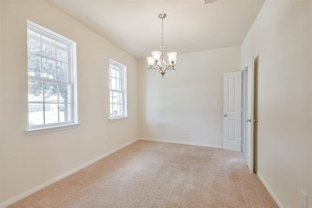Elegant formal dining room featuring a stunning chandelier, French doors to the kitchen and two large sets of windows, filling the space with natural light.