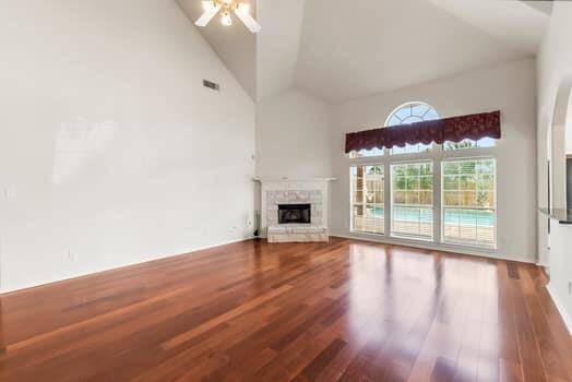 Spacious living room with high ceilings, featuring elegant wooden flooring and a cozy fireplace. Large windows provide abundant natural light and offer views of the beautiful pool.