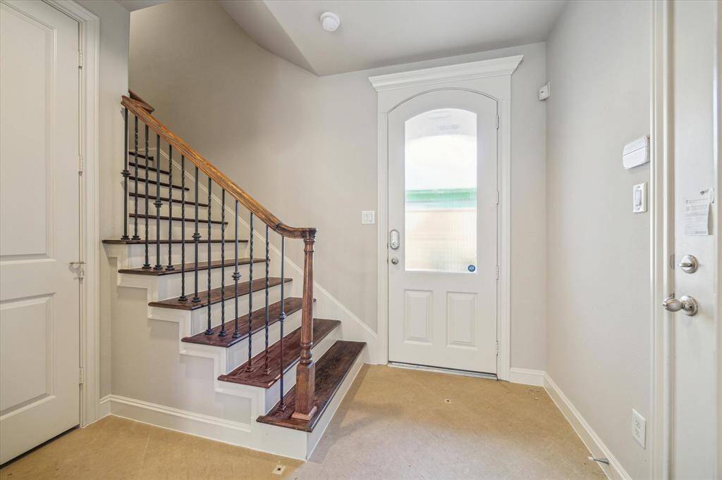 This photo features a bright entryway with a wooden staircase and wrought iron railing, leading to the upper floor. The space is well-lit and has a modern front door with frosted glass.