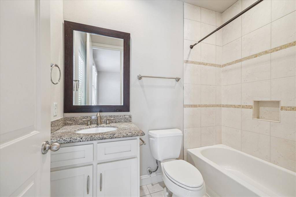 This is a modern bathroom featuring a granite-topped vanity with a framed mirror, a bathtub with tiled walls, and a built-in shower niche. The space is bright and well-lit.